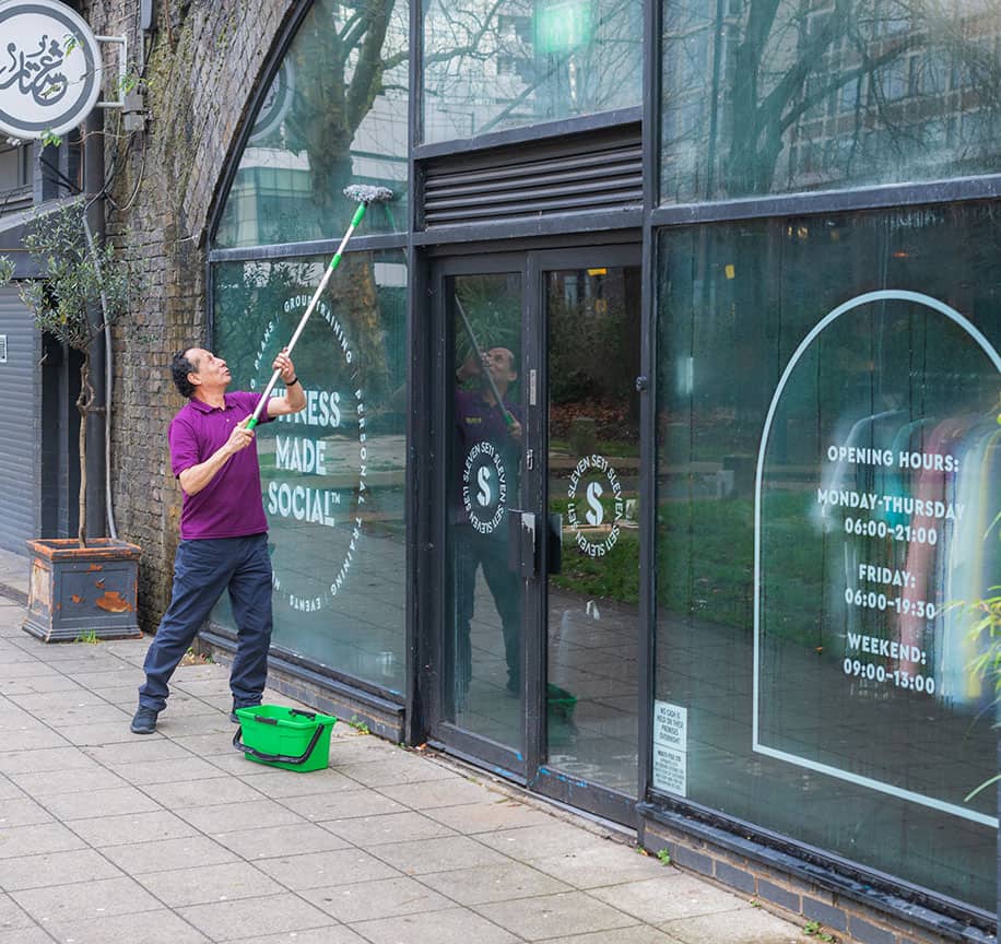 Professional window cleaner using a long pole to clean large glass windows.